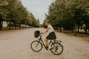 A joyful woman riding a bicycle along a tree-lined path in a Parisian park.